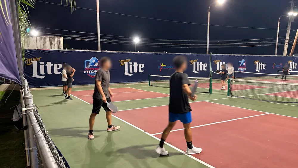 Vista nocturna de lonas en la valla de una cancha de pickleball, con datos privados ocultos